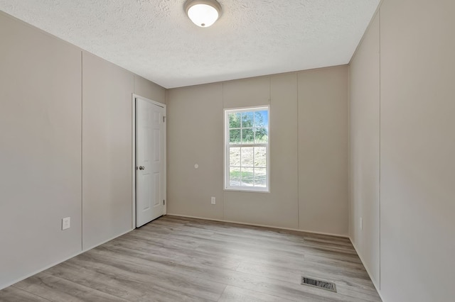 empty room with visible vents, a textured ceiling, and light wood finished floors