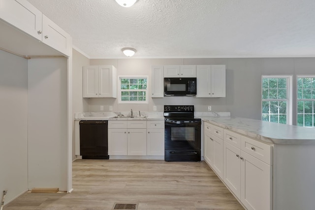 kitchen with a peninsula, a sink, white cabinetry, black appliances, and light wood finished floors