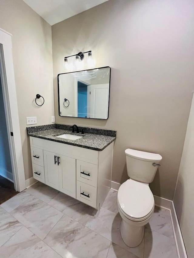 half bathroom with marble finish floor, vanity, and baseboards