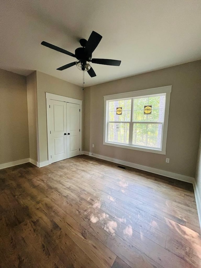 unfurnished bedroom featuring a closet, wood finished floors, a ceiling fan, and baseboards