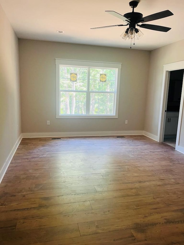 empty room featuring a ceiling fan, visible vents, baseboards, and wood finished floors