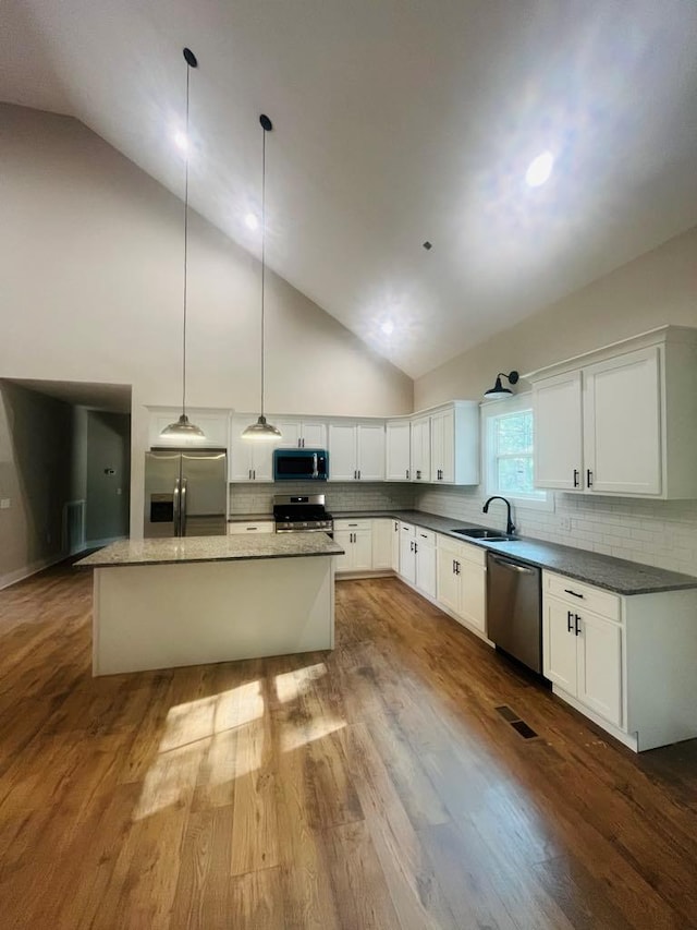 kitchen with a kitchen island, appliances with stainless steel finishes, decorative light fixtures, white cabinetry, and a sink