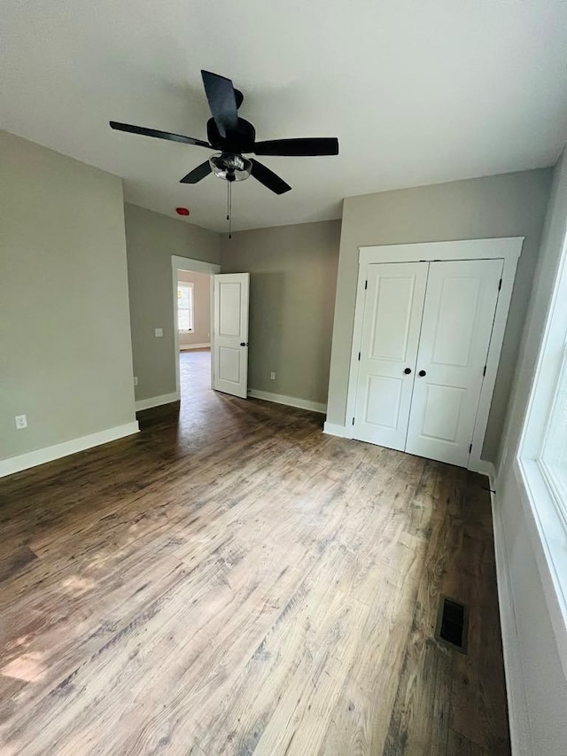 unfurnished bedroom with a closet, wood finished floors, visible vents, and baseboards