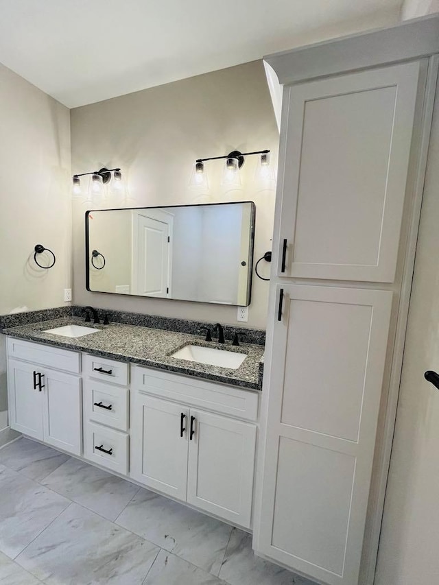 full bath featuring marble finish floor, double vanity, and a sink