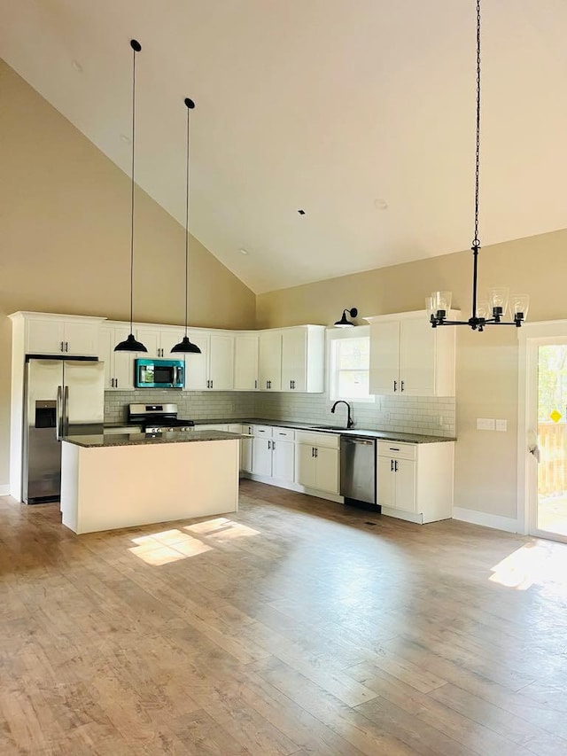 kitchen with a center island, pendant lighting, stainless steel appliances, dark countertops, and white cabinets