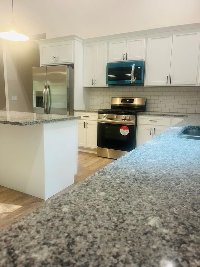 kitchen featuring stainless steel appliances, backsplash, white cabinets, light stone countertops, and light wood-type flooring