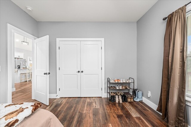 bedroom with a closet, dark wood-style flooring, baseboards, and stainless steel fridge with ice dispenser