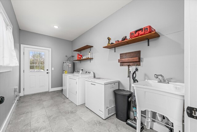 washroom with laundry area, a sink, baseboards, water heater, and washer and clothes dryer