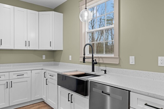 kitchen featuring light stone counters, pendant lighting, stainless steel dishwasher, white cabinetry, and a sink