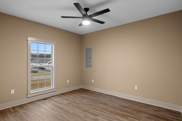 spare room featuring wood finished floors, visible vents, a ceiling fan, baseboards, and electric panel