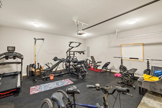 workout area featuring a garage, electric panel, a textured ceiling, and baseboards