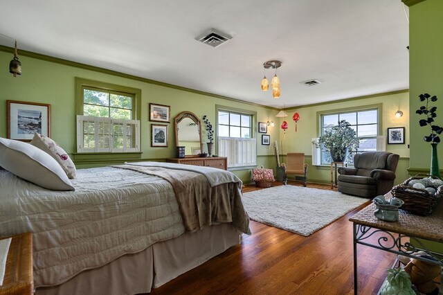 bedroom featuring ornamental molding, wood finished floors, visible vents, and multiple windows