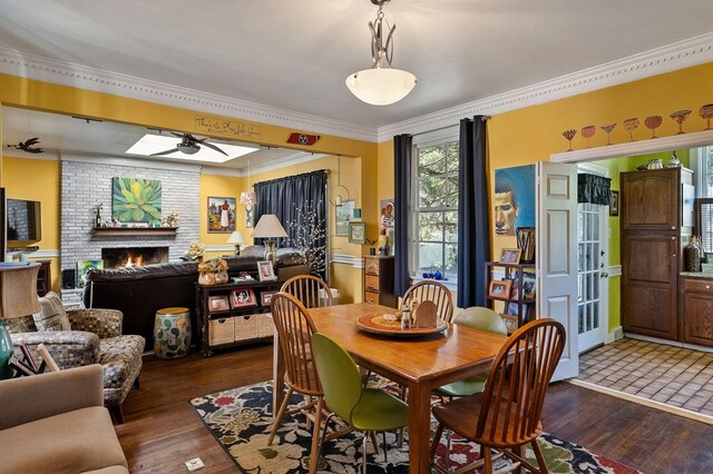 dining area featuring ornamental molding, dark wood-style flooring, a brick fireplace, and a ceiling fan