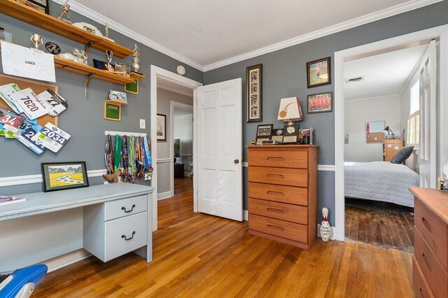 bedroom featuring built in desk, ornamental molding, and wood finished floors