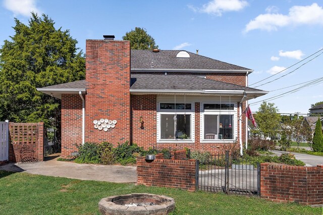 back of property with brick siding, roof with shingles, a chimney, fence, and a fire pit