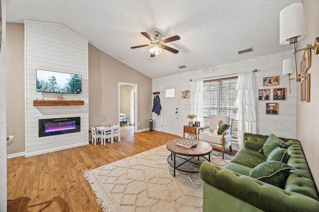 living area with lofted ceiling, a fireplace, wood finished floors, and visible vents