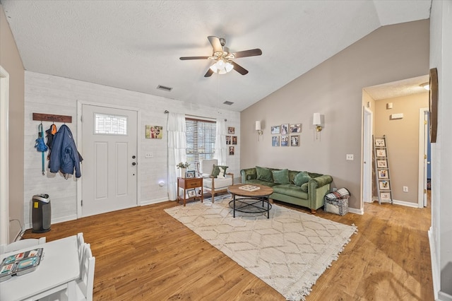 living room with a textured ceiling, visible vents, light wood-style floors, and vaulted ceiling