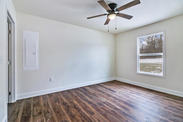 spare room featuring a ceiling fan, electric panel, dark wood finished floors, and baseboards