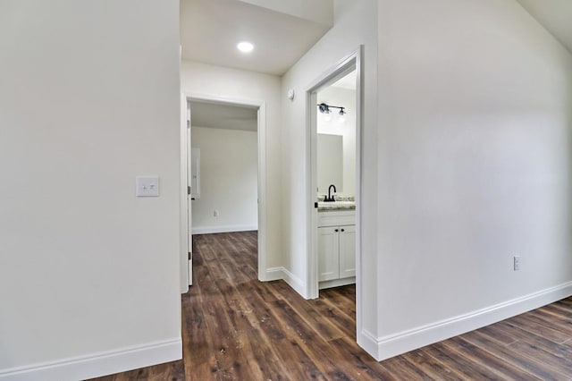 corridor featuring baseboards, dark wood finished floors, and a sink