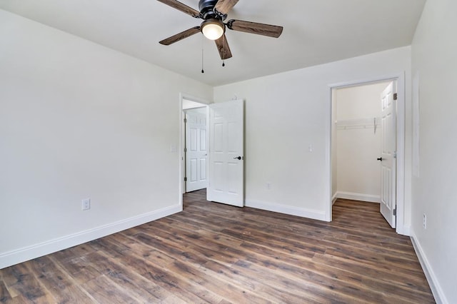 unfurnished bedroom featuring a spacious closet, dark wood-style flooring, a ceiling fan, and baseboards