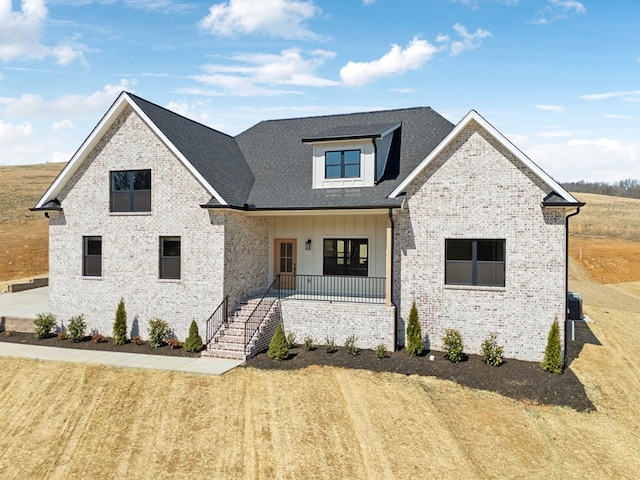 modern farmhouse style home featuring brick siding, board and batten siding, roof with shingles, covered porch, and cooling unit