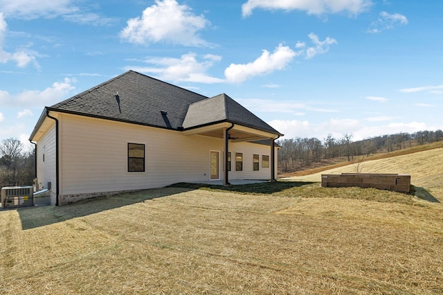 rear view of house featuring a patio, a yard, central AC unit, and a shingled roof