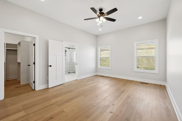 unfurnished bedroom featuring light wood finished floors, a walk in closet, baseboards, recessed lighting, and ensuite bath