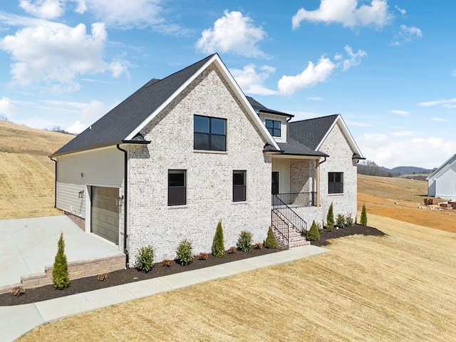 view of front of house with driveway, roof with shingles, a front lawn, a garage, and brick siding