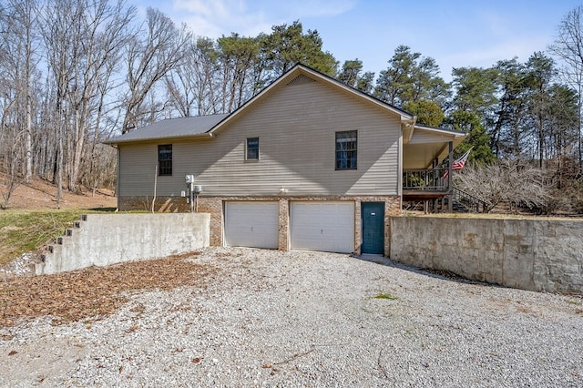 exterior space featuring a garage, gravel driveway, and brick siding