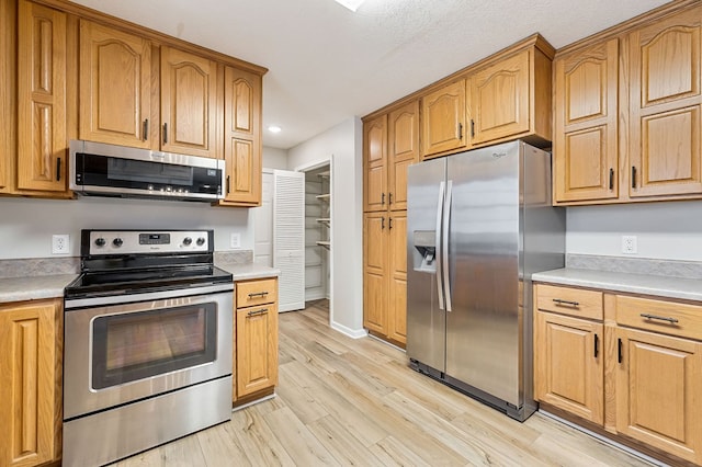 kitchen with stainless steel appliances, brown cabinets, light countertops, and light wood finished floors