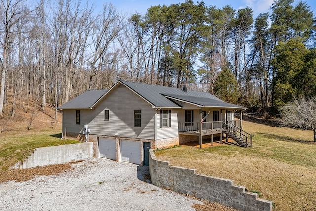 ranch-style home featuring covered porch, metal roof, a garage, driveway, and a front lawn