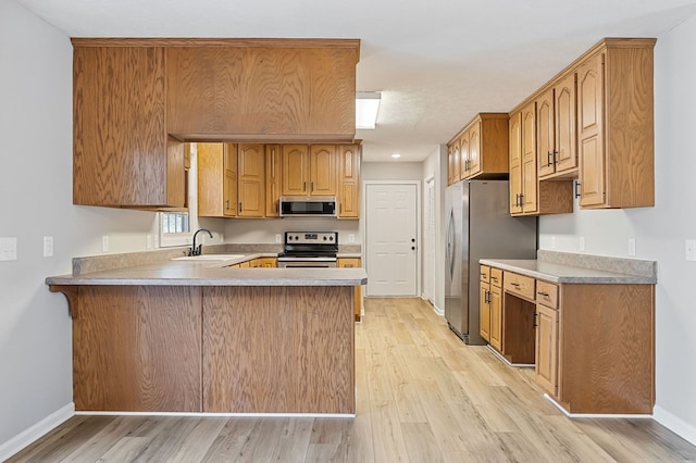 kitchen featuring stainless steel appliances, a peninsula, a sink, baseboards, and light wood finished floors