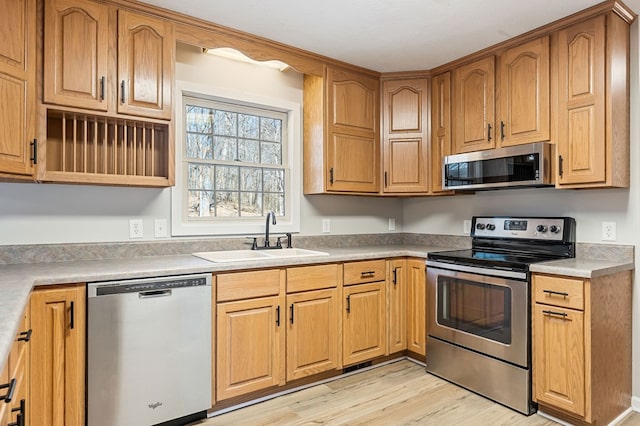 kitchen featuring open shelves, light countertops, appliances with stainless steel finishes, a sink, and light wood-type flooring