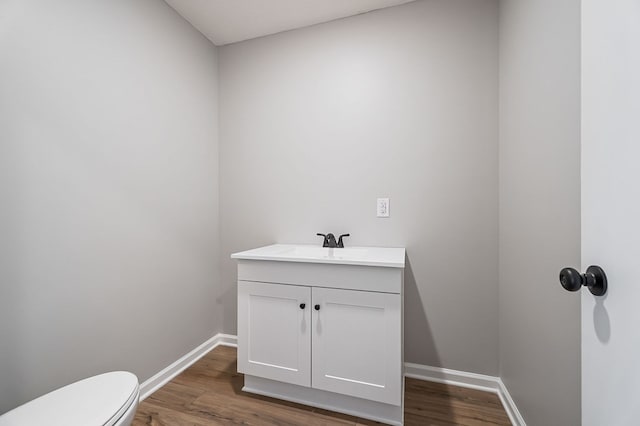 half bathroom featuring vanity, wood finished floors, toilet, and baseboards