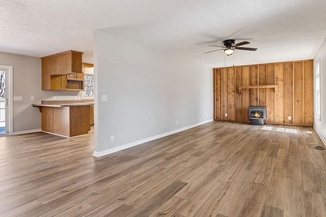 unfurnished living room featuring a textured ceiling, ceiling fan, wood walls, and wood finished floors