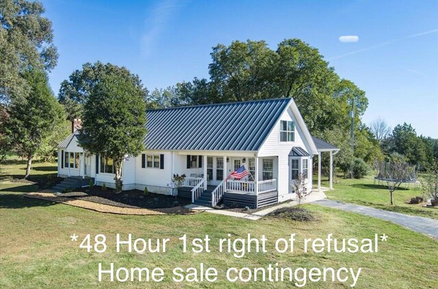 view of front of home with a porch, metal roof, a standing seam roof, a trampoline, and a front lawn