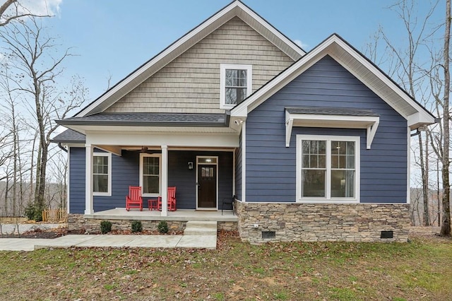 view of front of property featuring stone siding, a porch, crawl space, and roof with shingles