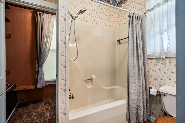 bathroom with stone finish floor, shower / bathtub combination with curtain, toilet, and wallpapered walls