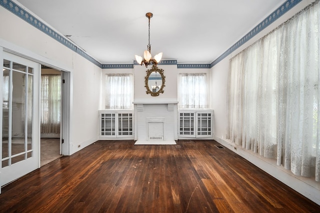 unfurnished living room with dark wood-style floors, crown molding, a fireplace, an inviting chandelier, and baseboards