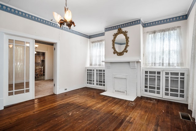 unfurnished living room with baseboards, visible vents, dark wood-type flooring, an inviting chandelier, and a fireplace