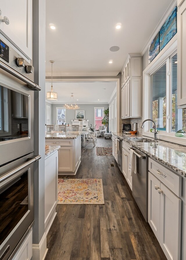 kitchen featuring pendant lighting, stainless steel appliances, a sink, and white cabinets