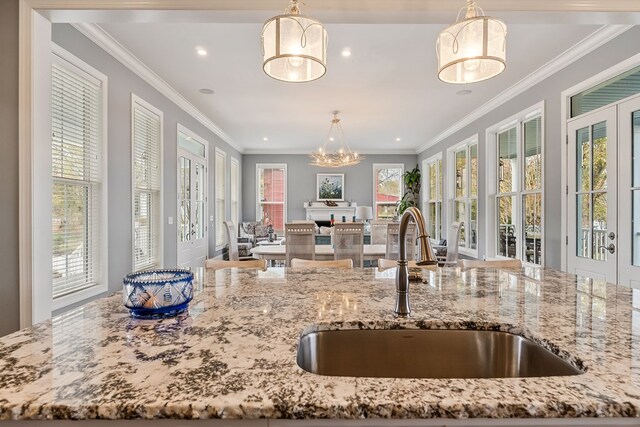 kitchen with light stone counters, a sink, and decorative light fixtures