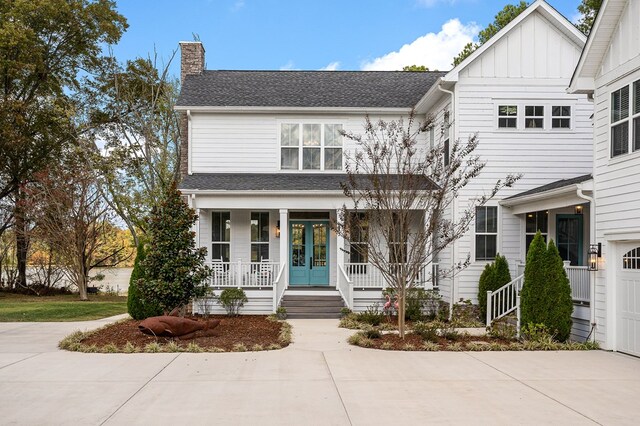 view of front of house with french doors, roof with shingles, a chimney, a porch, and board and batten siding