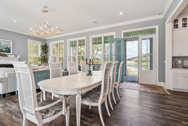 dining area featuring a notable chandelier, a fireplace, a water view, ornamental molding, and dark wood-style floors