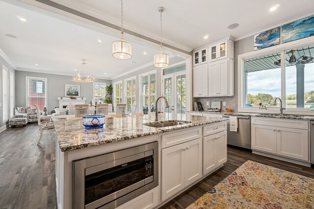 kitchen featuring a center island with sink, decorative light fixtures, stainless steel appliances, white cabinetry, and a sink