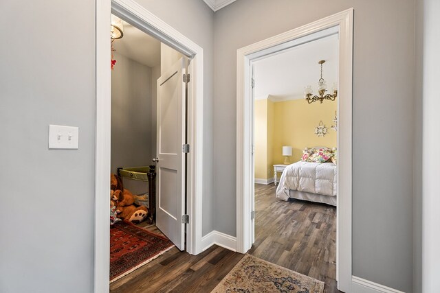 hallway featuring dark wood-style floors, ornamental molding, baseboards, and an inviting chandelier