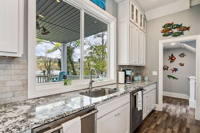 kitchen featuring stainless steel dishwasher, glass insert cabinets, white cabinets, a sink, and light stone countertops