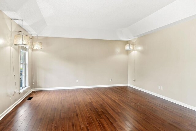 spare room with dark wood-type flooring, visible vents, and baseboards