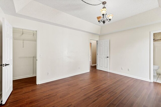 unfurnished bedroom featuring a closet, a walk in closet, dark wood-style flooring, and baseboards