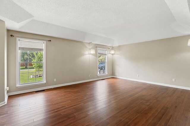 empty room featuring a wealth of natural light, dark wood-style flooring, and a textured ceiling